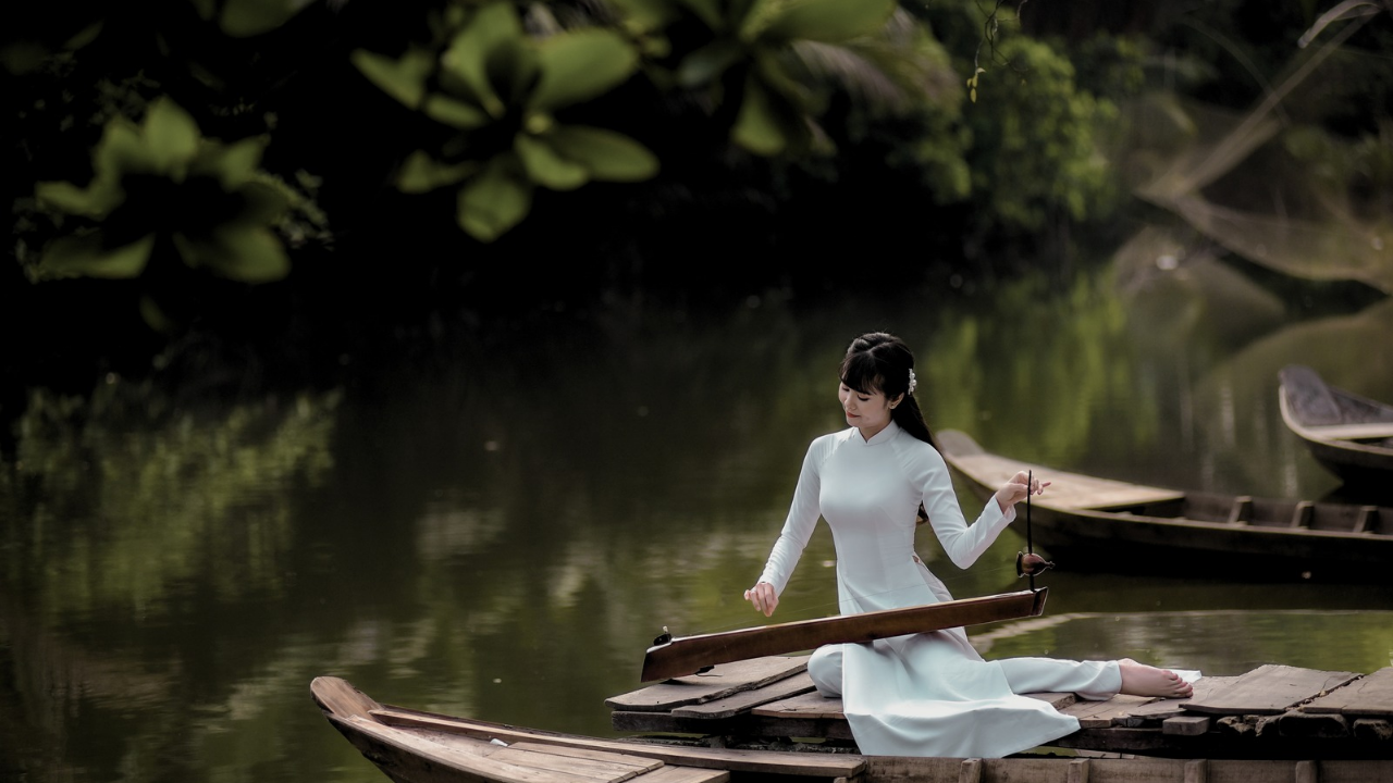Mujer entre la naturaleza llena de vegetación , arbustos y arboles en medio de un lago con una canoa.